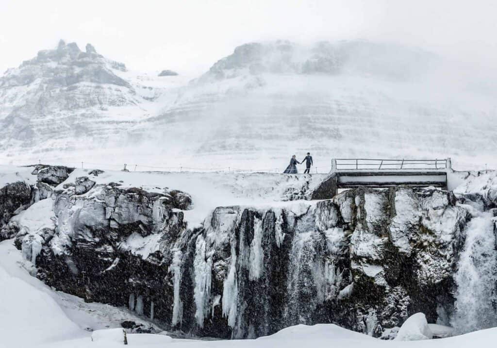 A wedding couple crossing a bridge in snow, Icelandic winter.