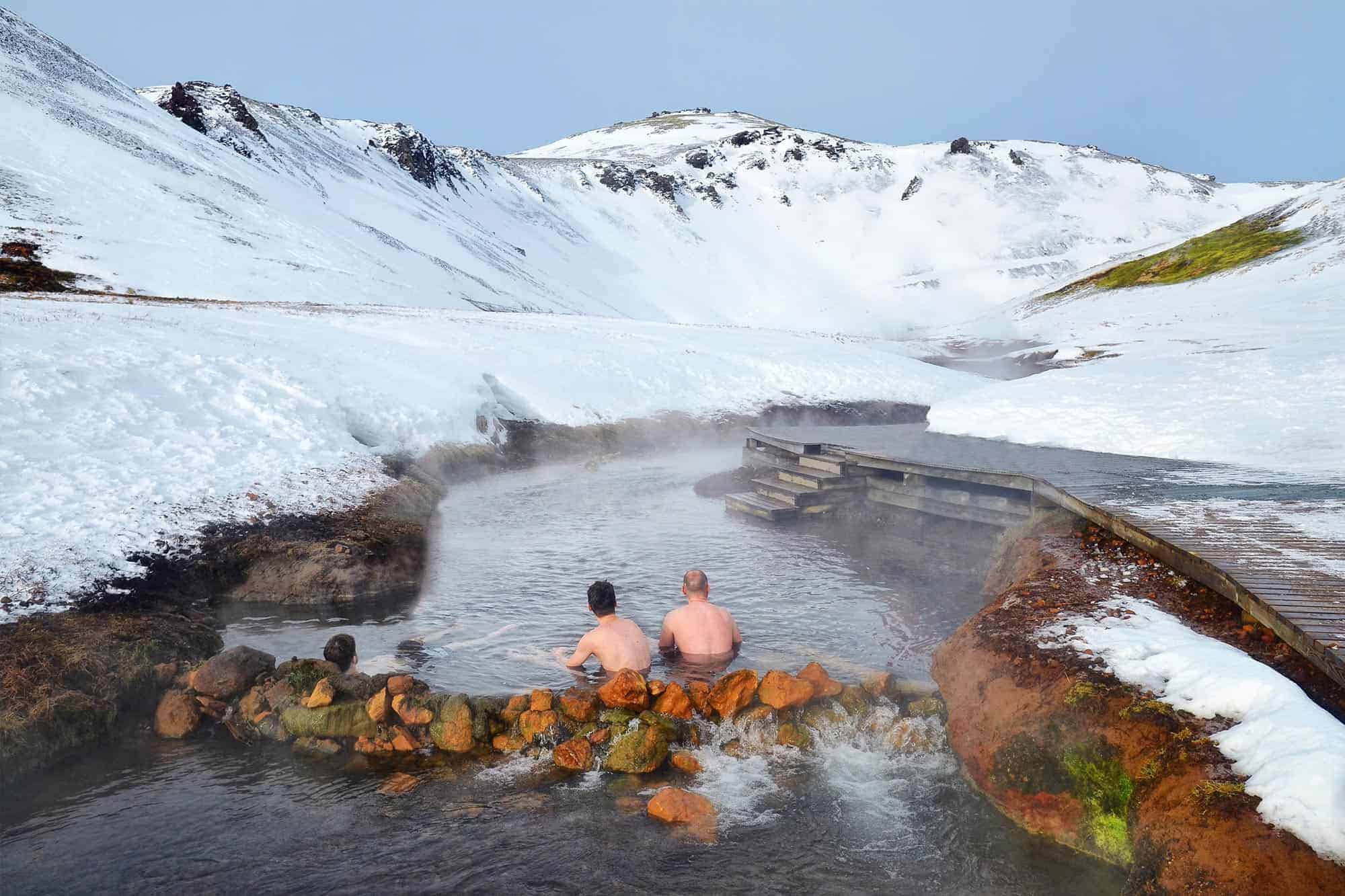 Three men soak in the Reykjadalur Hot Spring Thermal River in south Iceland on a snowy winter's day.
