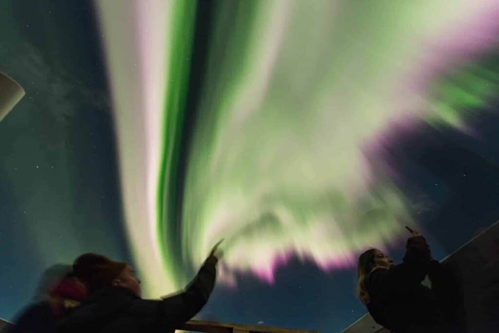 Guests at Hotel Rangá gaze up into the night sky filled with green and pink northern lights.