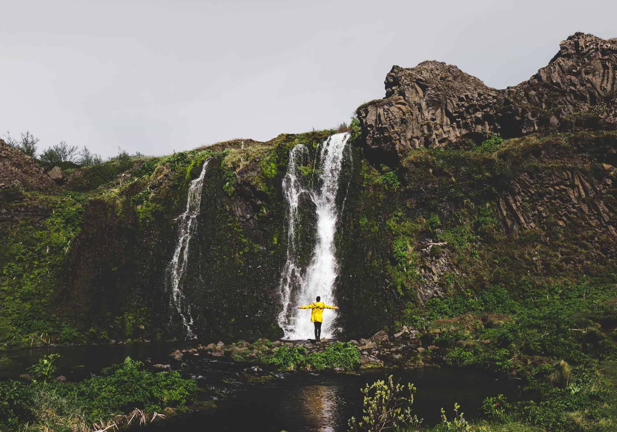 Girl in a yellow rain jacket stands in front of a waterfall in south Iceland.