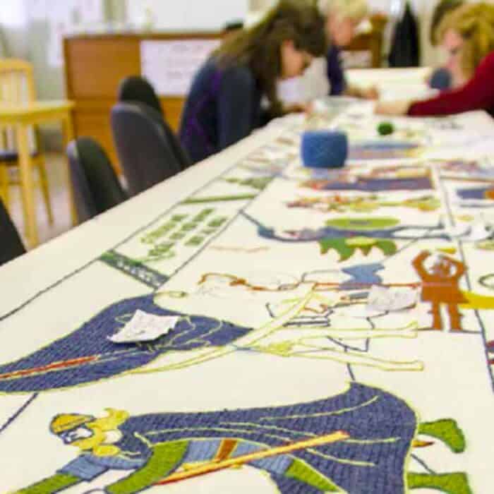 Women sew a traditional Icelandic tapestry covered with scenes from Njál's saga.