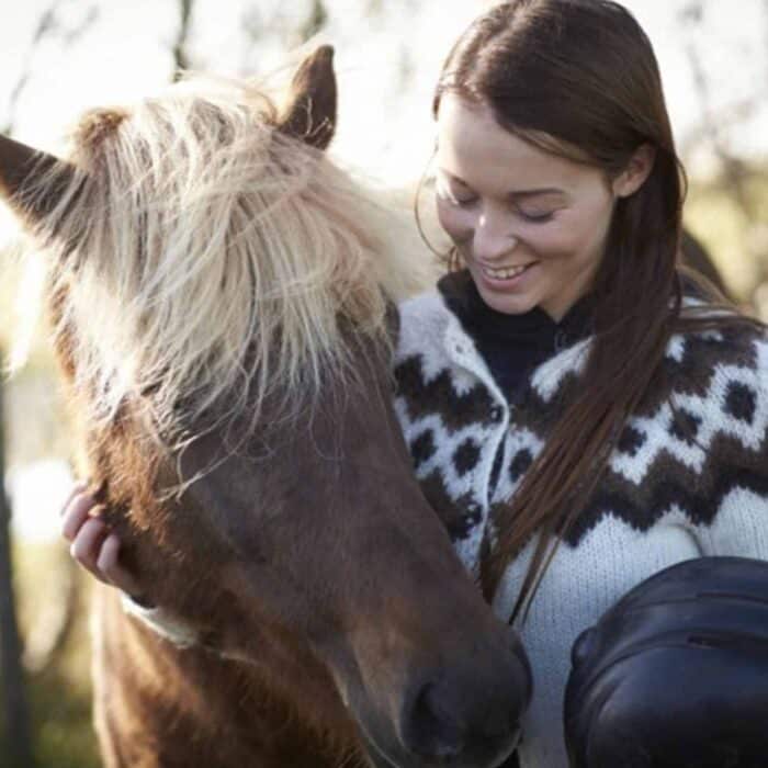 Woman wearing white Icelandic lopapeysa pets an Icelandic horse.