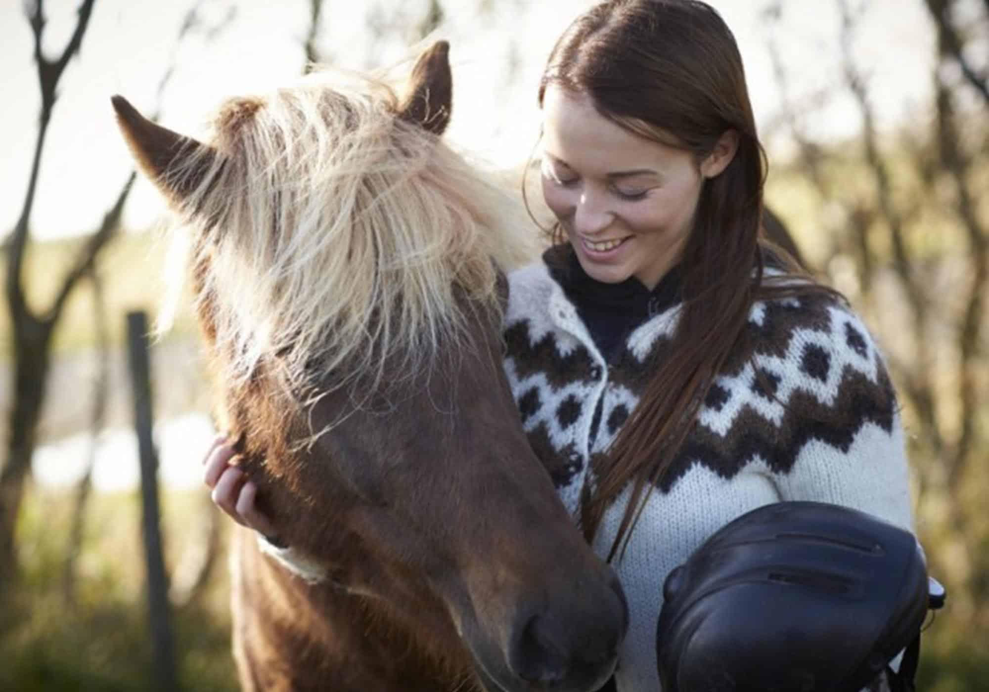 Woman wearing white Icelandic lopapeysa pets an Icelandic horse.