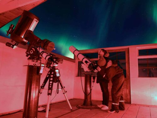 Guest looks through telescope into the night sky filled with northern lights in Hotel Rangá's Observatory.