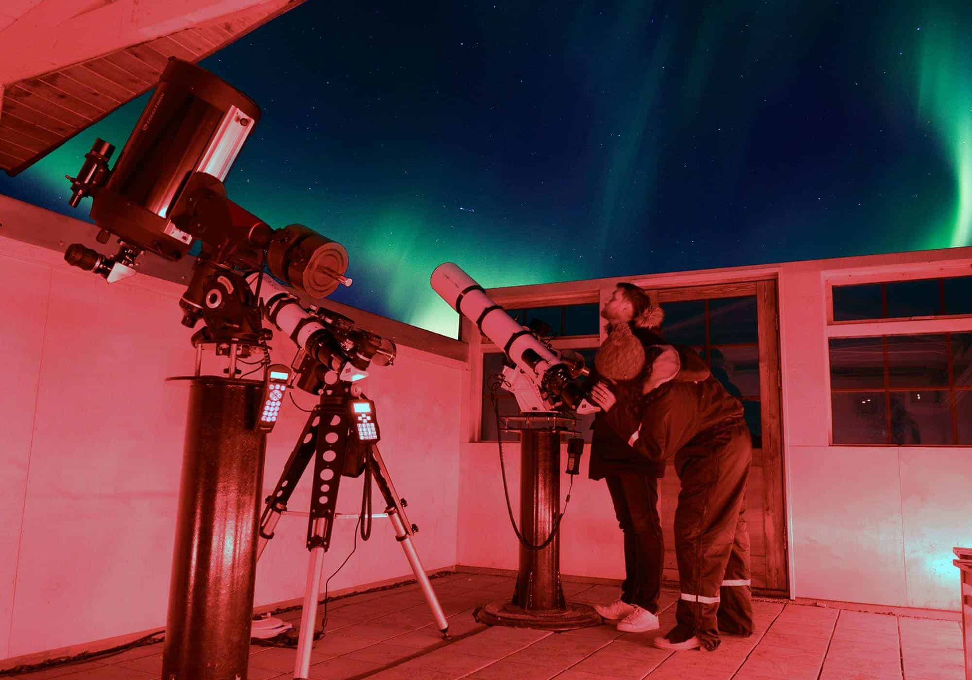 Guest looks through telescope into the night sky filled with northern lights in Hotel Rangá's Observatory.