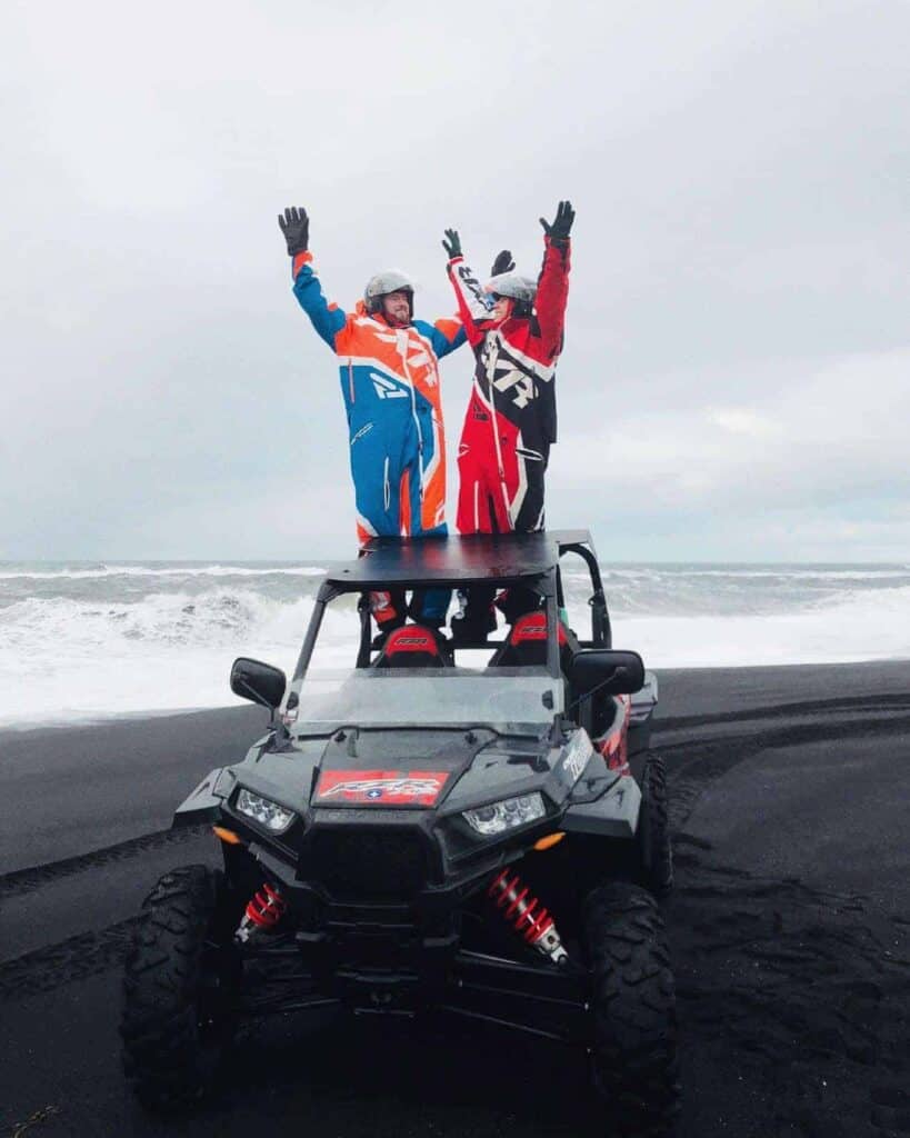 Two men stand atop a buggy on a black sand beach in Iceland.