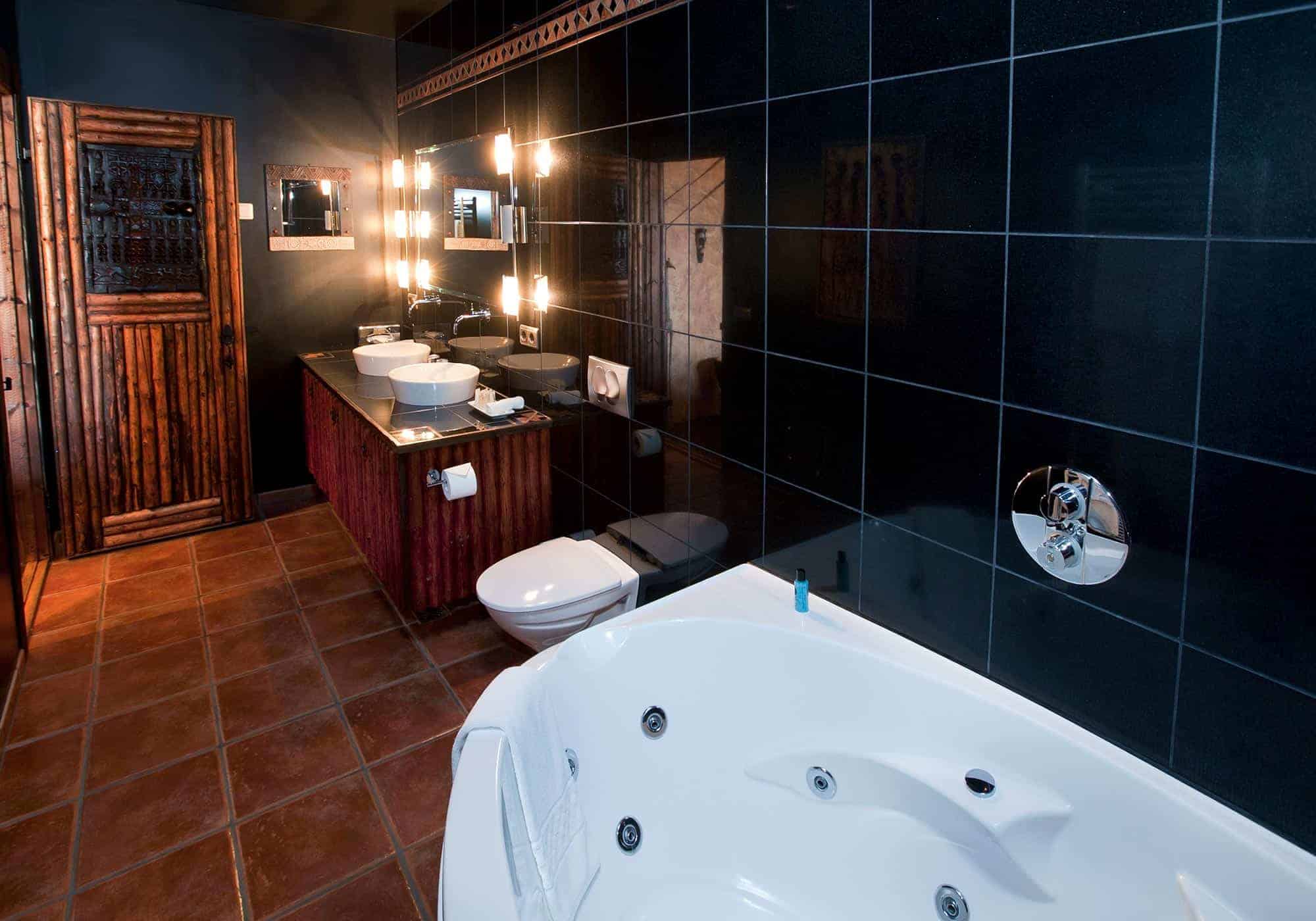 Bathroom in Hotel Rangá's Africa Master Suite decorated with black wall tile and large bathtub.