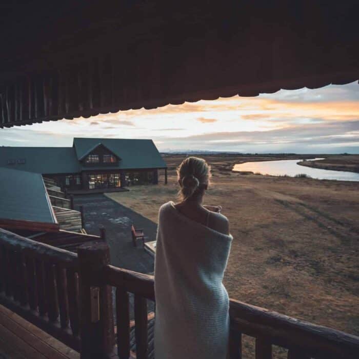 Woman wrapped in blanket stands on Hotel Rangá balcony overlooking the Rangá River at sunrise.
