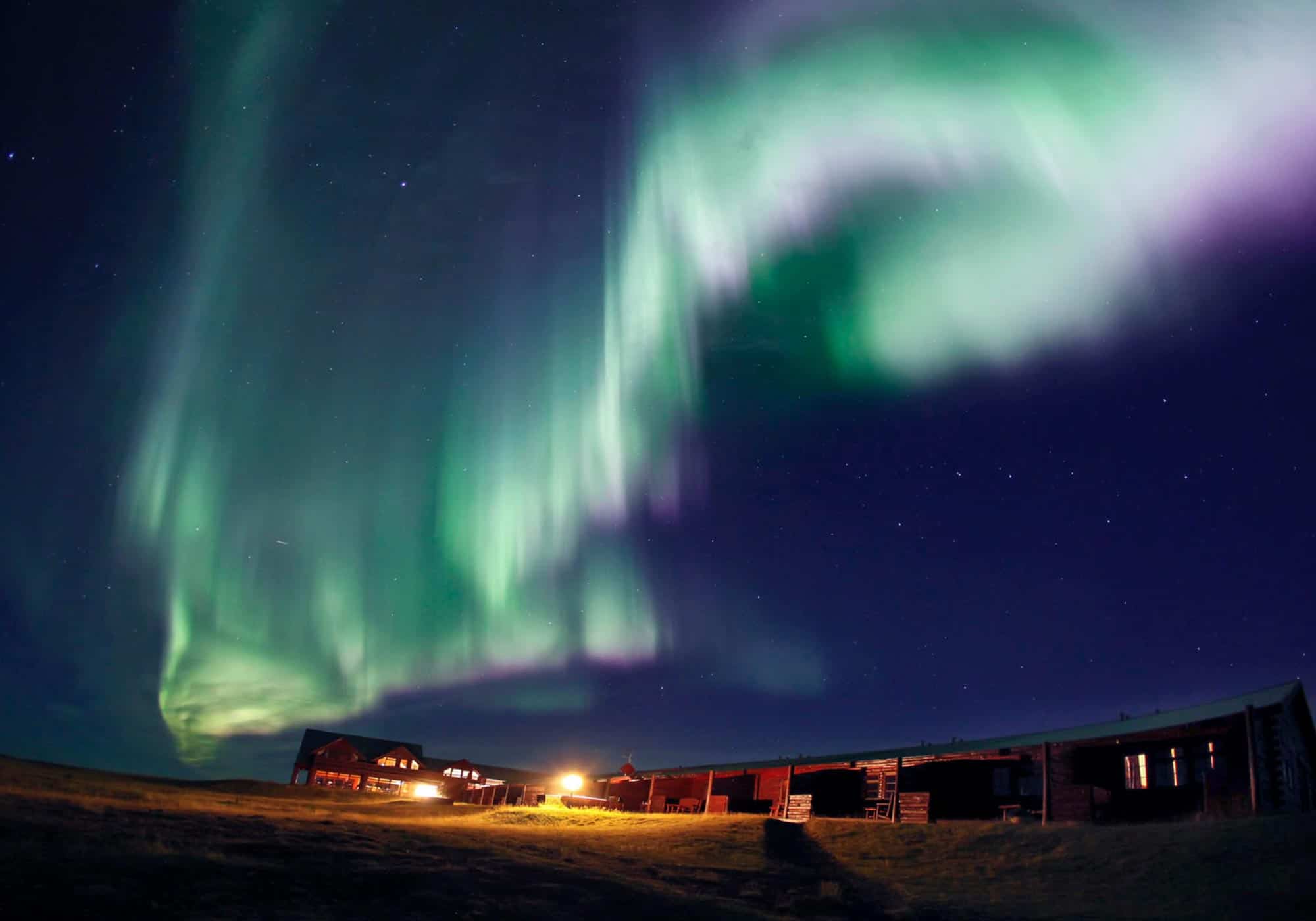 Green and pink northern lights above Hotel Rangá in south Iceland.