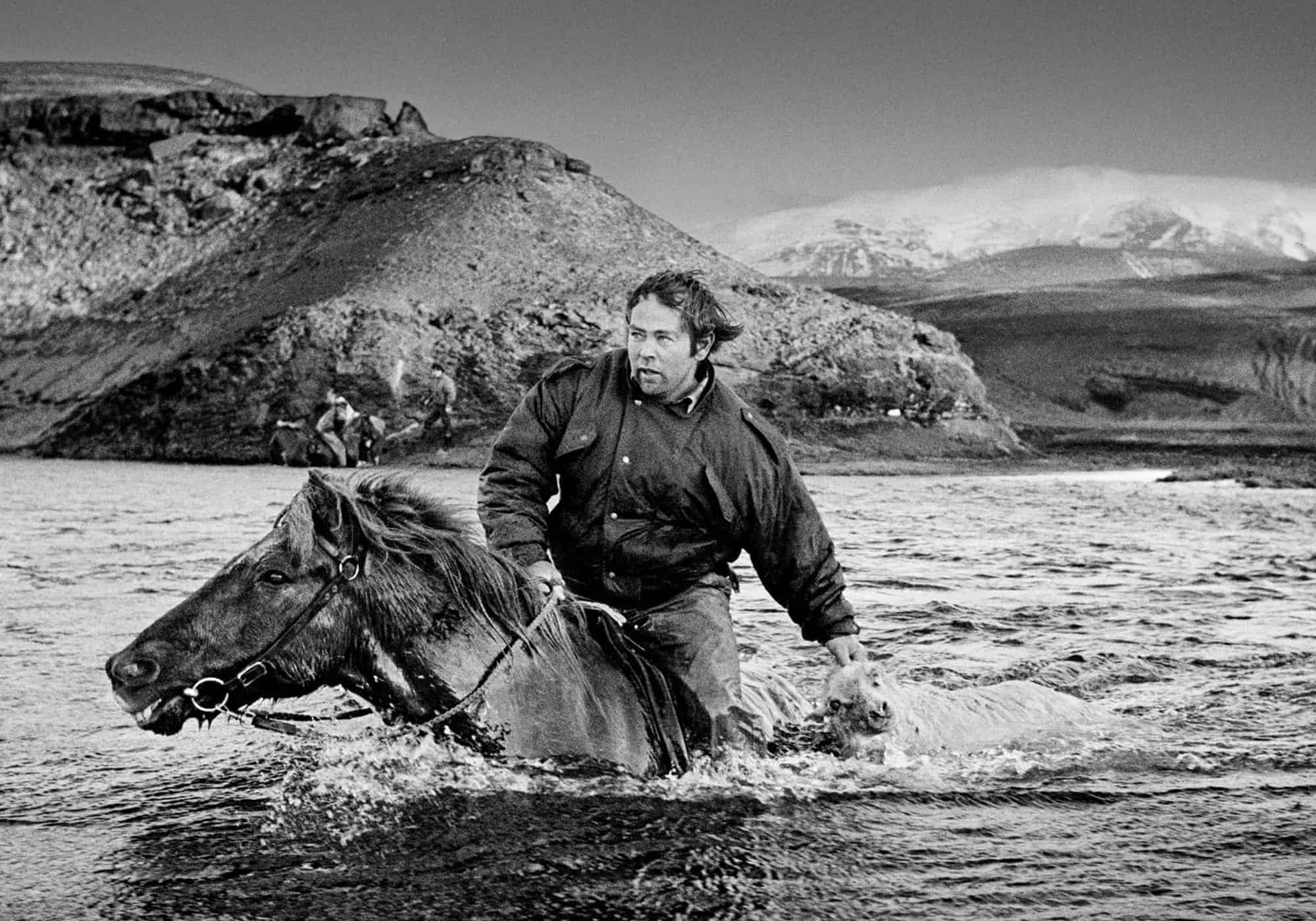 Man on horseback crossing a deep river in the arctic.