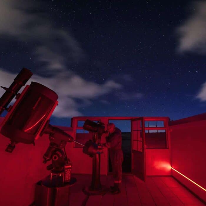 Man peers through telescope in Hotel Rangá Observatory underneath a starry night sky.