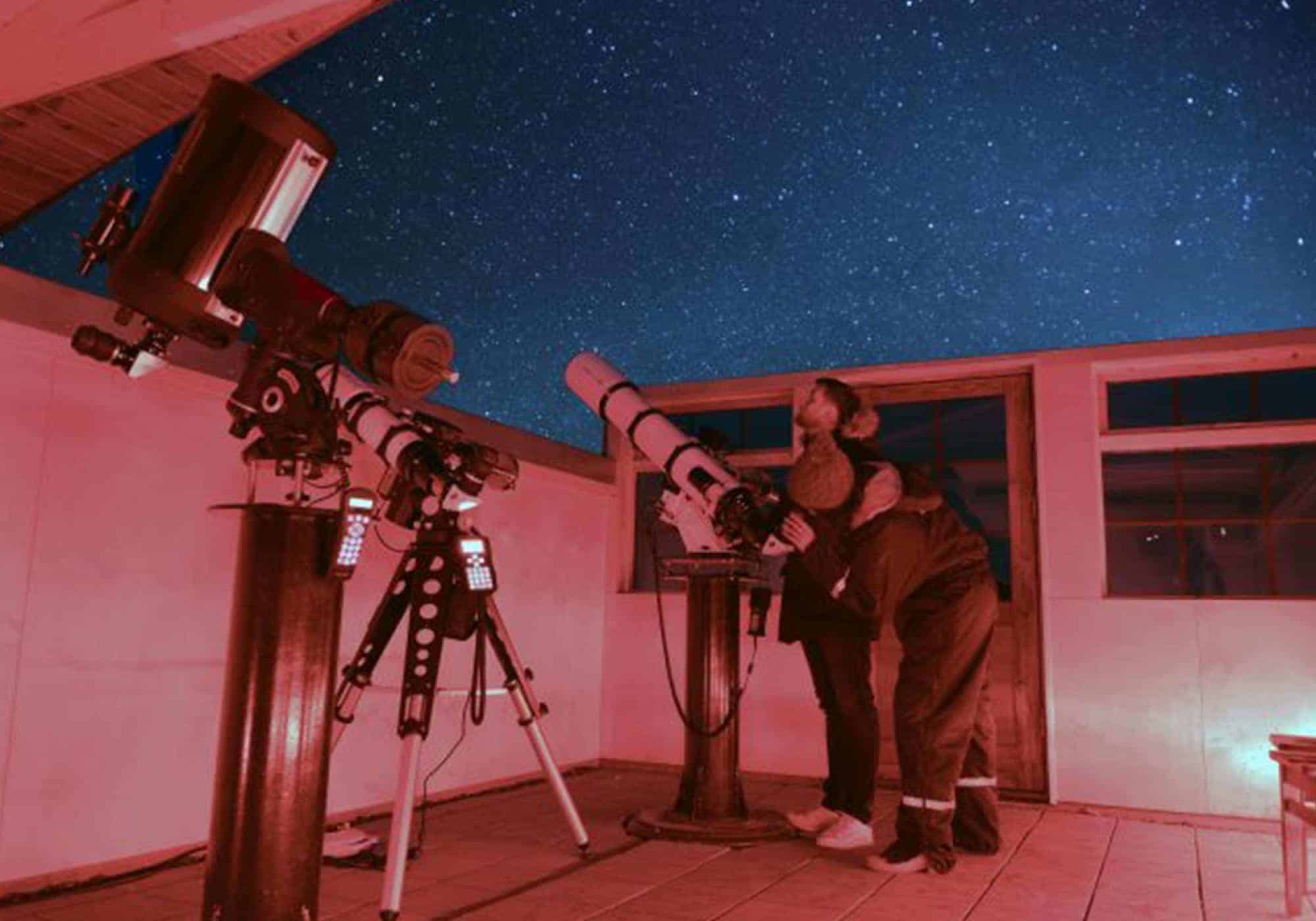 A woman peers through a telescope and a man stares into the starry night sky in the Rangá Observatory in south Iceland.