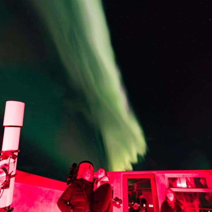 Guests stare into the night sky at green northern lights while standing in the Hotel Rangá Observatory.