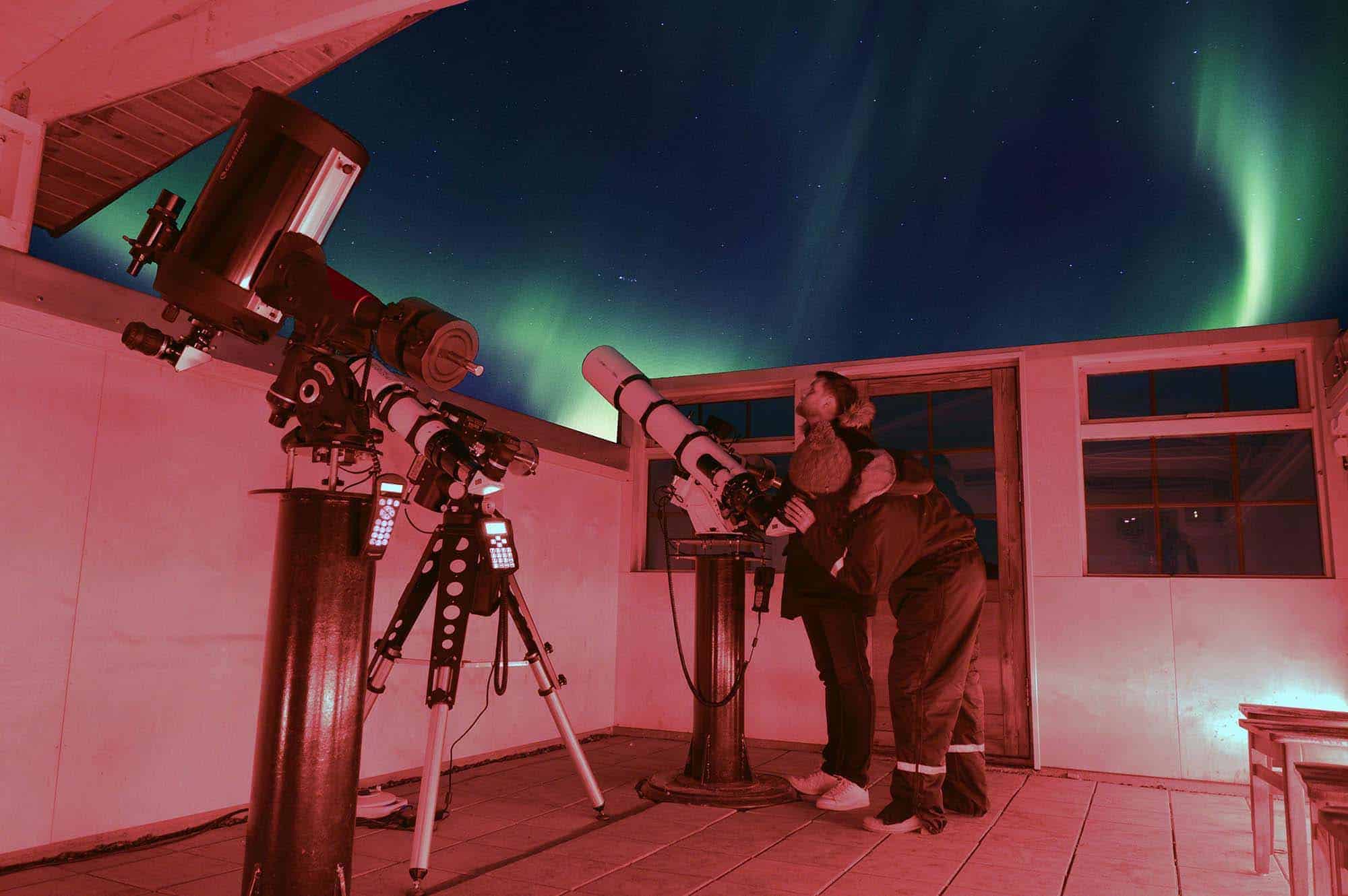 Woman stargazing in the Hotel Rangá Observatory underneath green northern lights.
