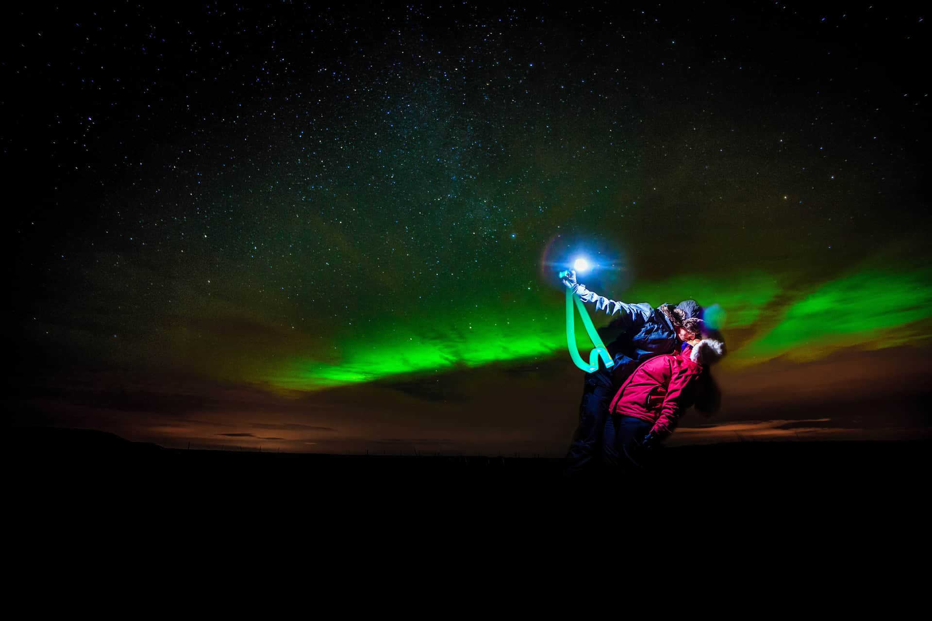 Couple embraces underneath the green northern lights in south Iceland.