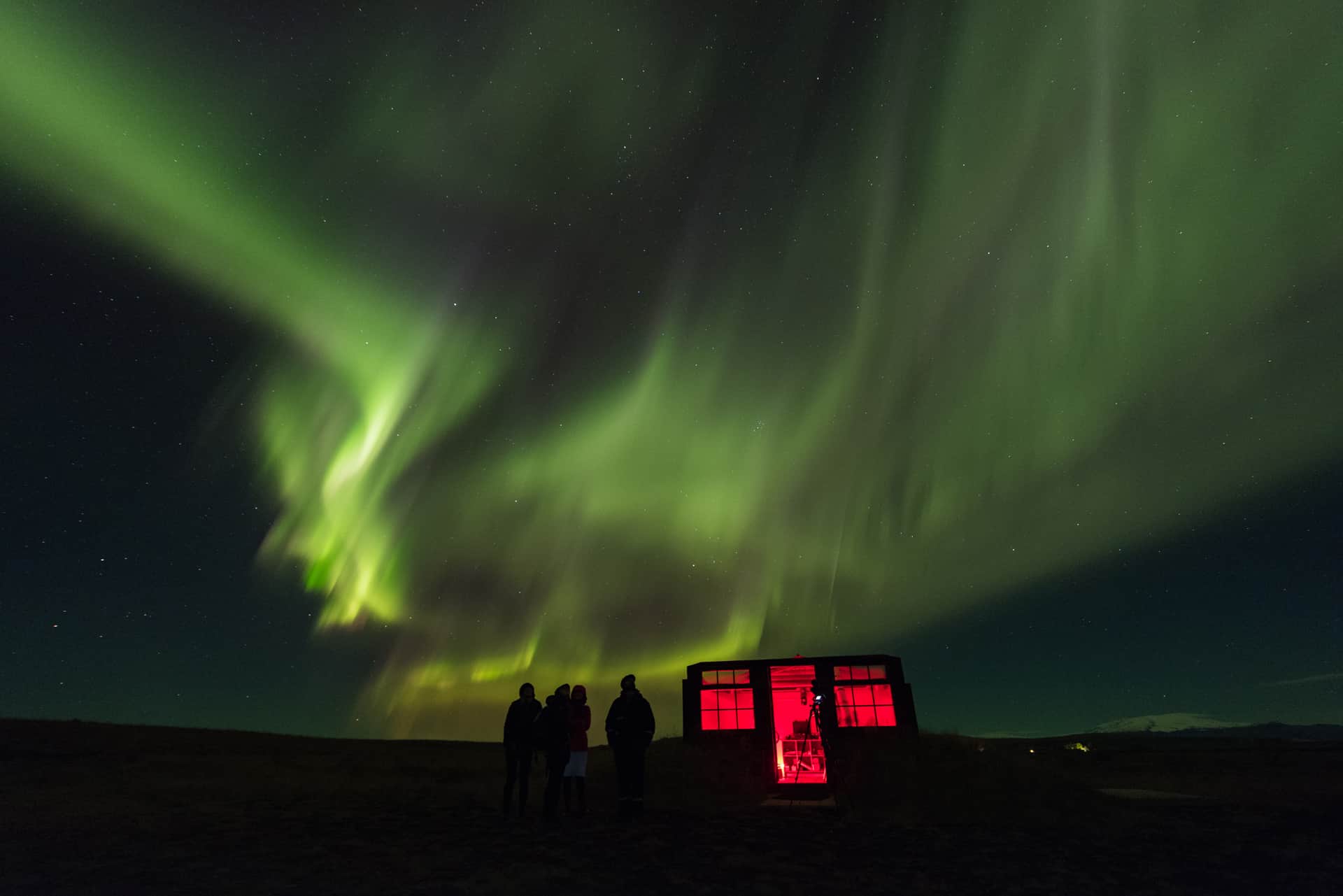 Green northern lights dance and swirl above a group of visitors outside the Hotel Rangá Observatory.