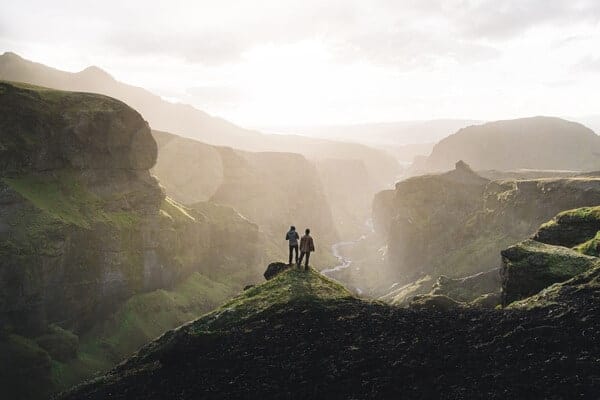 Two hikers stand on a grassy outcropping on the Fimmvörðuháls trail while hiking in Iceland.