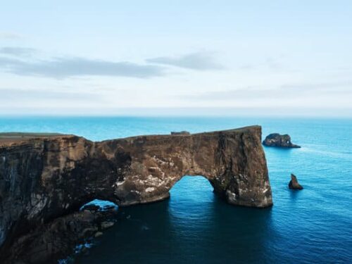 The Dyrhólaey promontory stretching out into the sea with a giant arch underneath the stone outcropping.