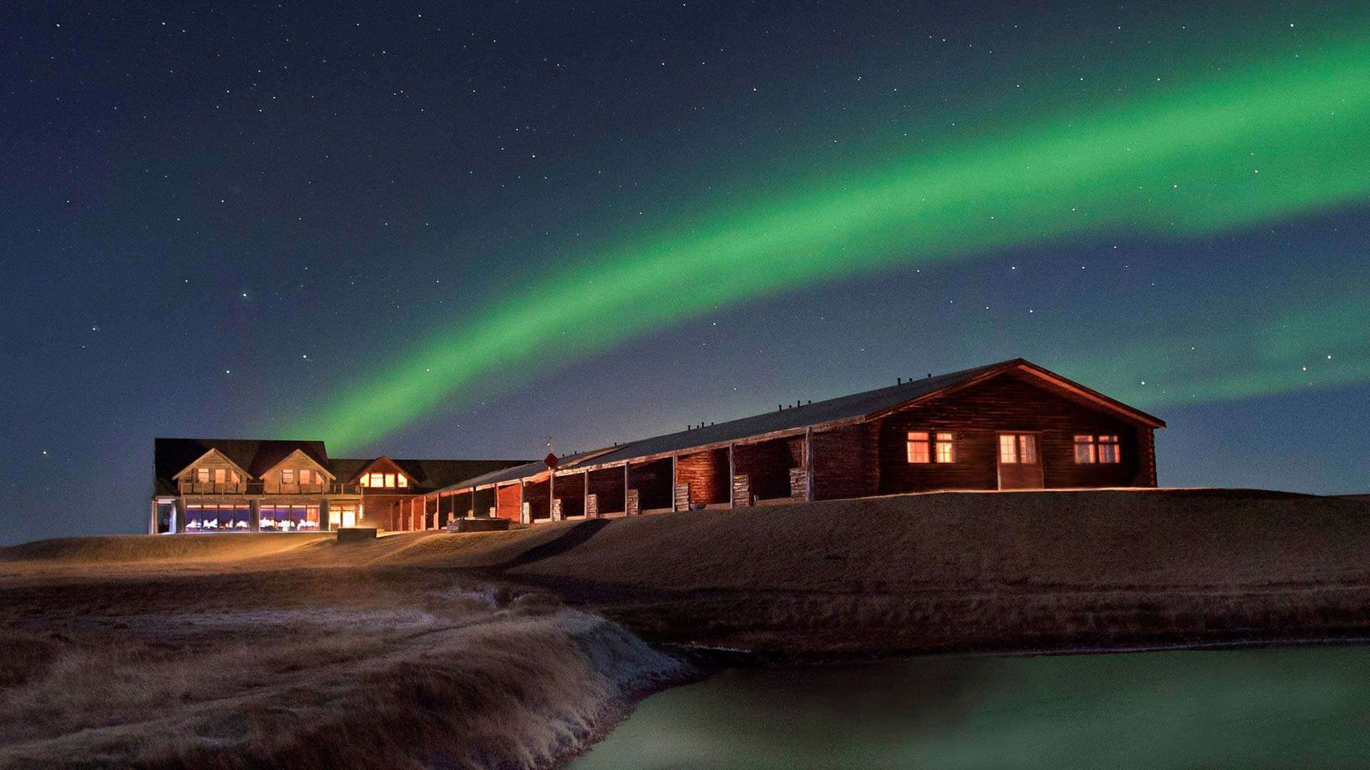 Hotel Rangá, a wooden lodge style building over which there are stars and green northern lights.