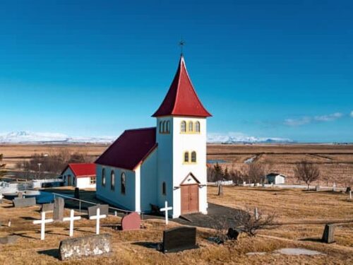 Oddakirkja church - a white building with a red roof - underneath a blue sky.