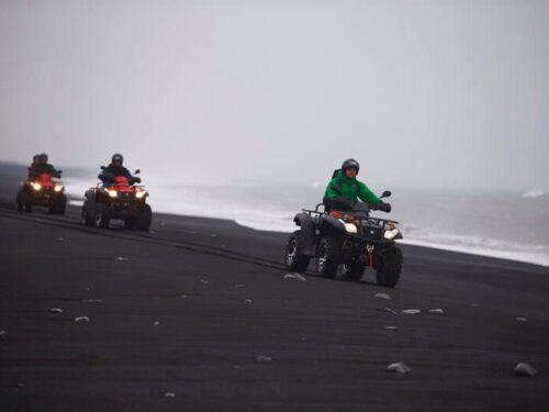 Several people drive on ATVs across a black sand beach in south Iceland.