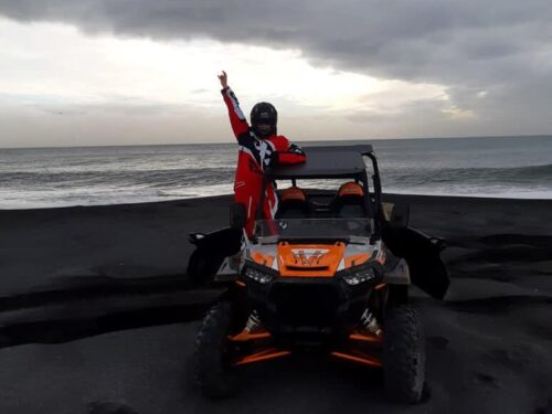 Man stands atop buggy on black sand beach in front of the ocean in south Iceland.