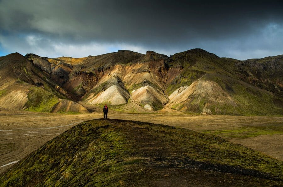 Hiker stands on a grassy knoll looking out onto the mountains of Landmannalaugar.