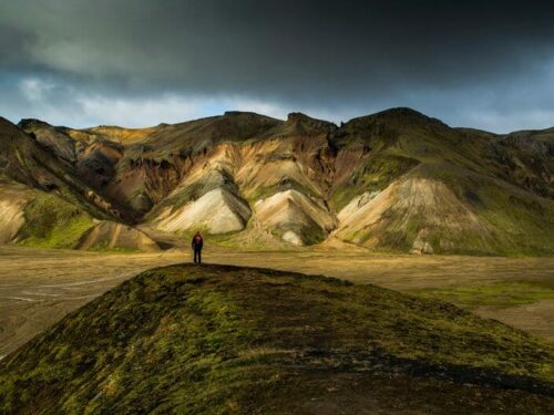 Hiker stands on grassy knoll in the Icelandic highlands.