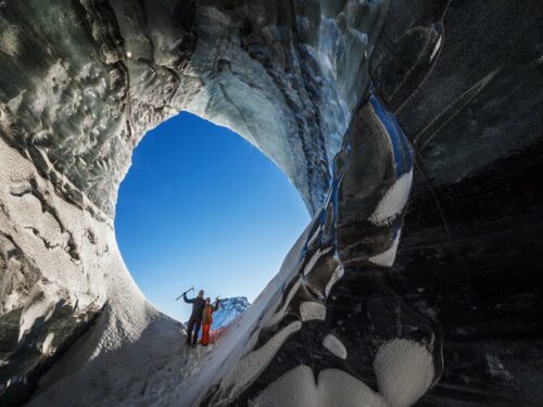 Couple stands in the entrance to an ice cave looking out onto south Iceland.