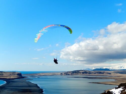 People paragliding over a black sand beach in Vík
