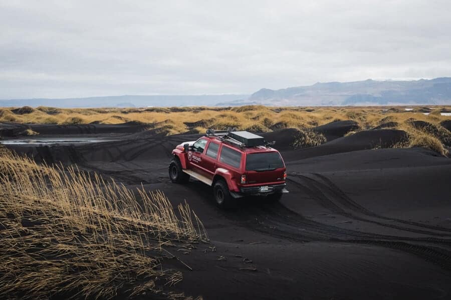 Red super jeep drives across a black sand beach in south Iceland.