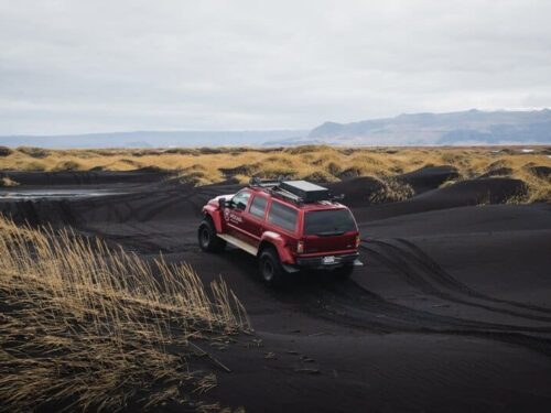 Red Super Jeep drives over black sands in south Iceland.