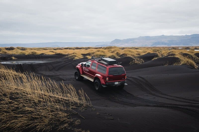 Red Super Jeep drives over black sands in south Iceland.