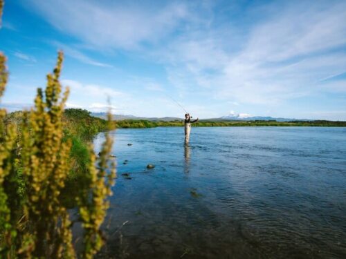 Fisherman stands in the Rangá River and casts his rod with a view of Eyjafjallajökull in the background.