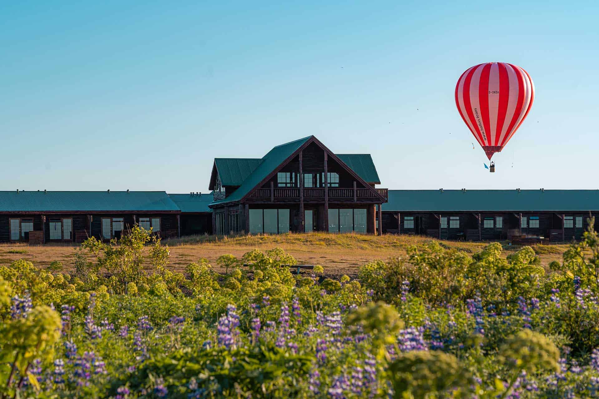 Red and pink hot air balloon over the exterior of Hotel Rangá with purple lupine flowers in the foreground.