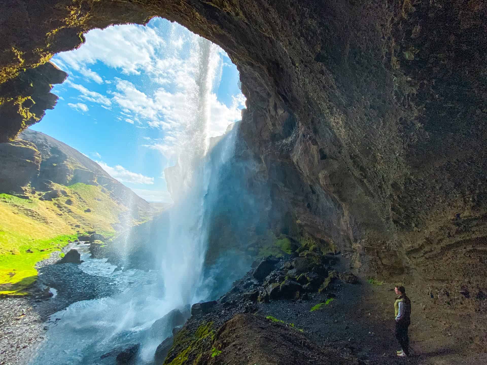 Woman stands behind Kvernufoss waterfall in south Iceland.