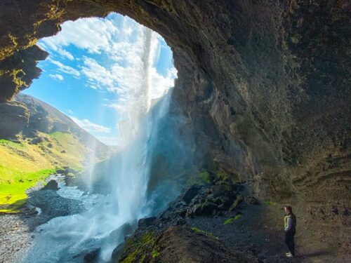 Woman walks underneath Kvernufoss waterfall in south Iceland.