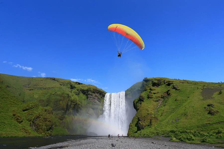 Paragliders over Skógafoss waterfall in south Iceland under a clear blue sky.