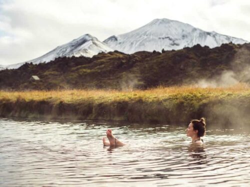 Woman lounges in a hot spring underneath snow-covered mountains.