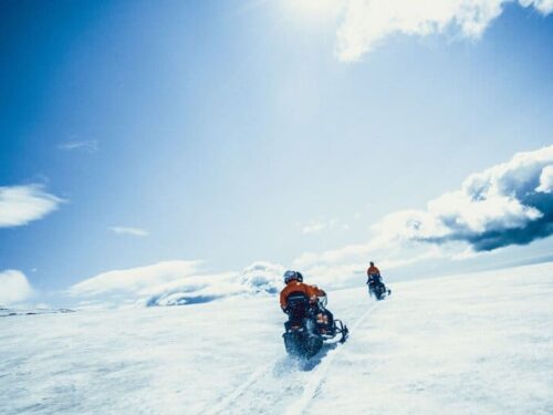 Two snowmobiles whizzing across the Eyjafjallajökull glacier underneath sun and blue skies.