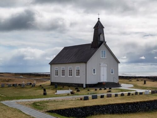 Strandakirkja church covered in white siding and a black roof with views of the ocean nearby.