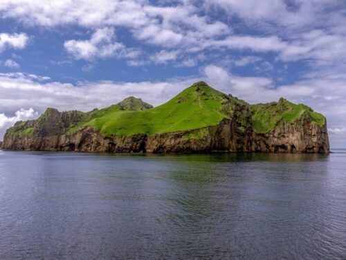 The Westman Islands covered with green grass under a blue sky filled with white clouds.