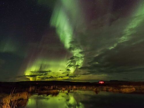 Green northern lights behind clouds over the Rangá Observatory.