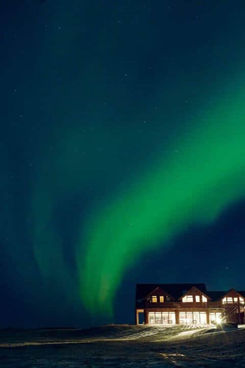 Green northern lights in a dark night sky above Hotel Rangá in south Iceland.