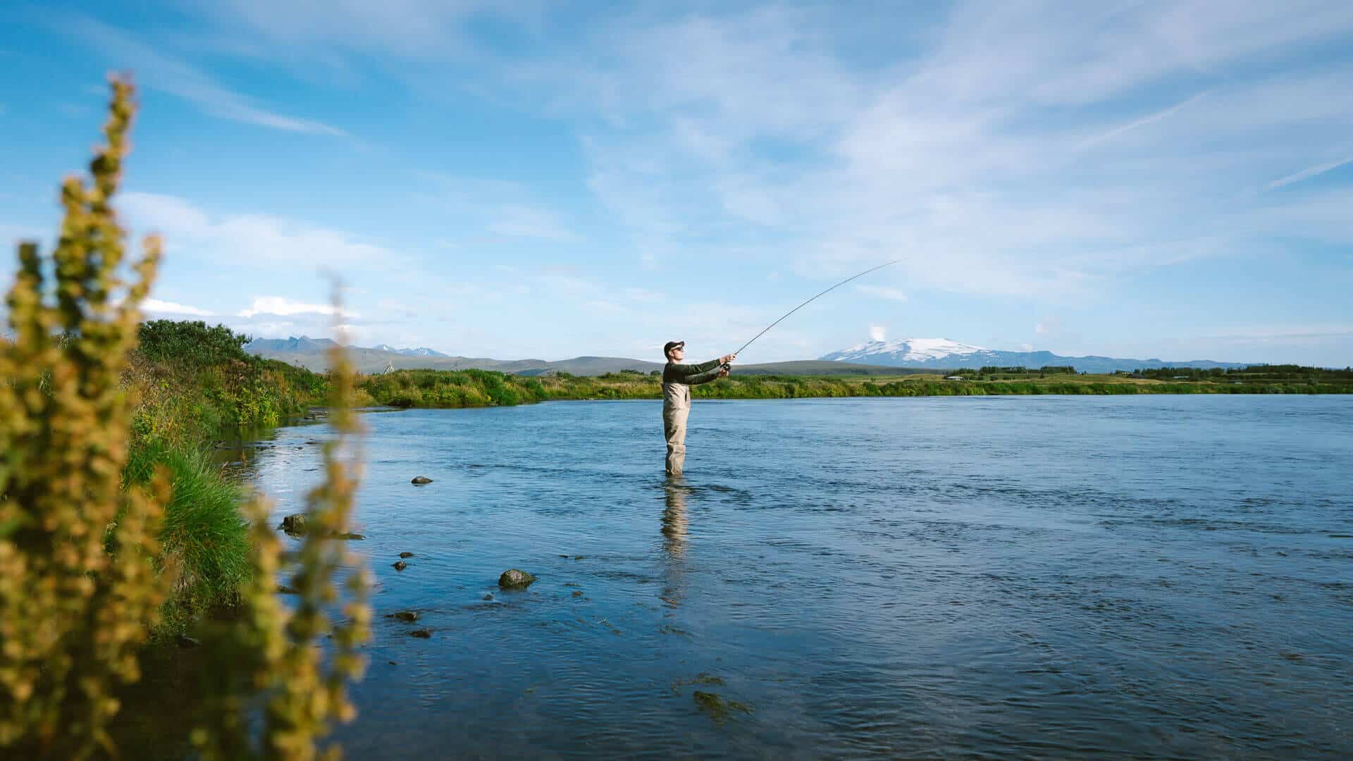 Fisherman wearing waders stands in the Rangá River as he casts his rod.