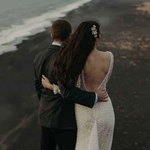 Wedding couple embraces atop the Dýrholaey promontory with views of a black sand beach.