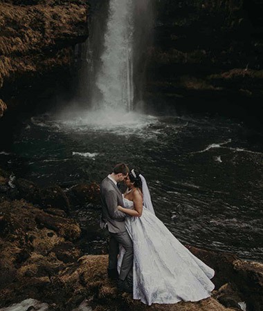 Wedding couple embrace underneath Gluggafoss waterfall.