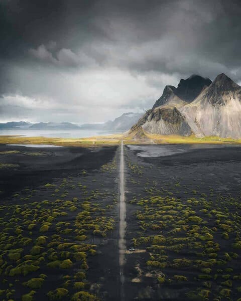 Overhead view of a country road in south Iceland with mountains and ocean in the background.