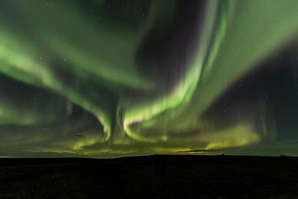 Bands of green northern lights with pink edges swirl through the night sky in south Iceland.