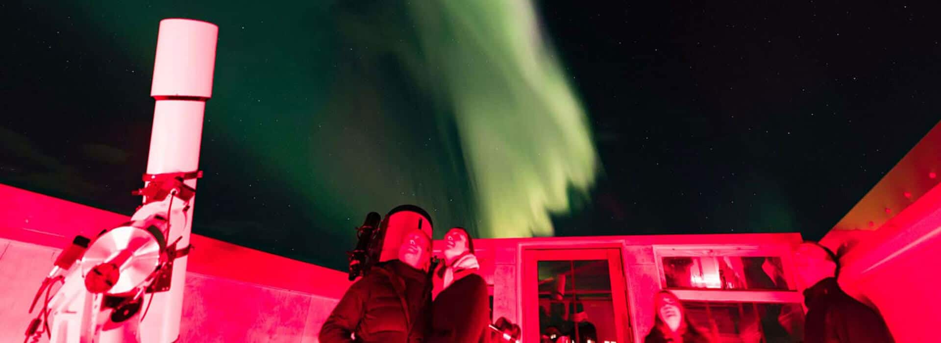 Visitors look up into the sky while standing in the Rangá Observatory as green northern lights are visible overhead.